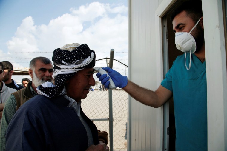 Image: A member of the medical team checks the temperature of a man, following the coronavirus outbreak, at the entrance checkpoint of Erbil