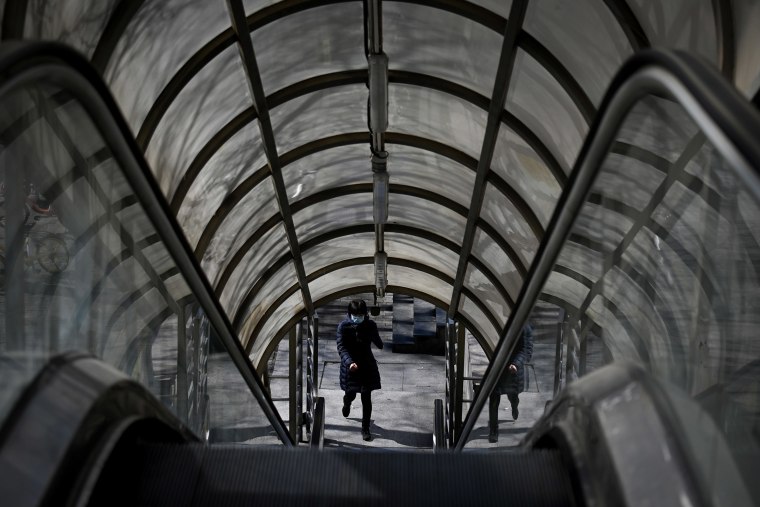 Image: A woman wearing a face mask uses an escalator in Beijing on Tuesday.