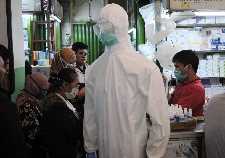 Image: A mannequin in protective suit is displayed as people buy masks and hand sanitizers at a market in Jakarta, Indonesia