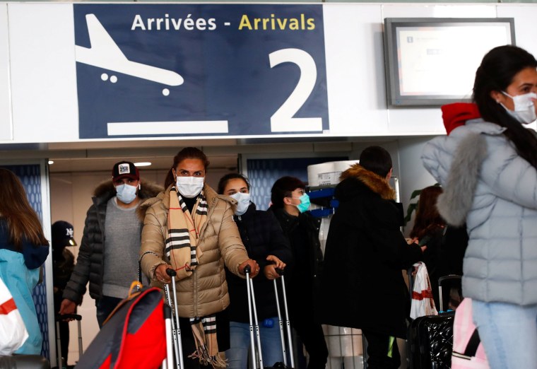 Image: People wearing protective face masks walk at as they arrive at Charles de Gaulle airport in Paris