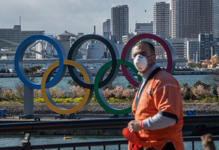 Image: A man wearing a face mask walks near the Olympic Rings in Odaiba on March 5, 2020 in Tokyo, Japan.