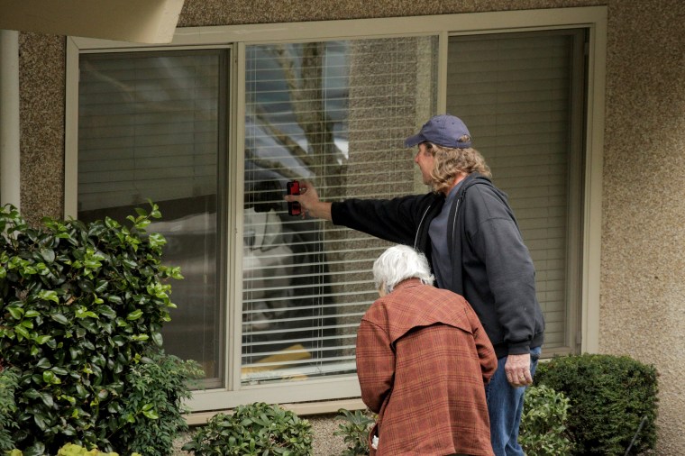 Image: Dorothy Campbell and her son, Charlie, talk through a window with her husband, Gene, at the Life Care Center of Kirkland, the long-term care facility linked to several confirmed coronavirus cases in Washington, on Thursday.