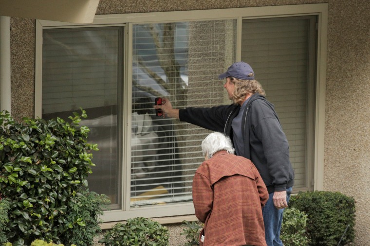 Image: Dorothy Campbell and her son, Charlie Campbell, talk through a window with her husband, Gene Campbell, at the Life Care Center of Kirkland, the long-term care facility linked to several confirmed coronavirus cases in the state, in Kirkland