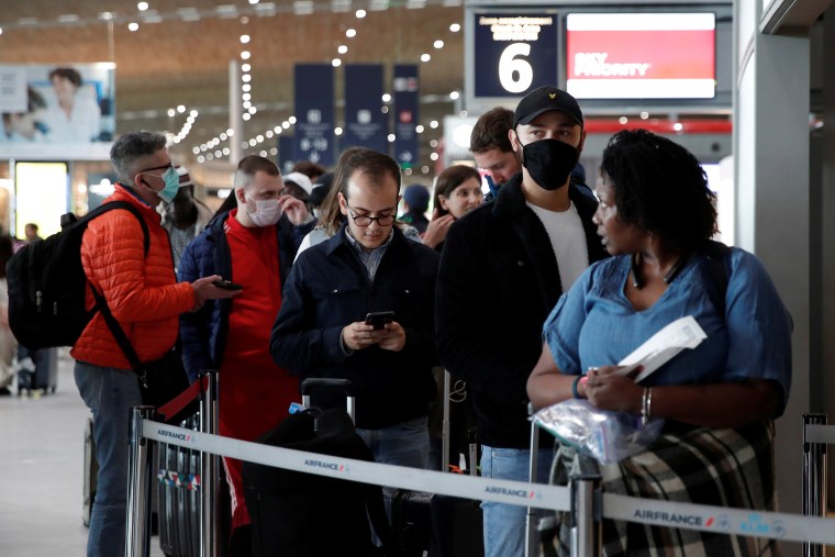 Image: People wearing protective face masks line up at the Air France ticketing desk inside Terminal 2E at Paris Charles de Gaulle airport
