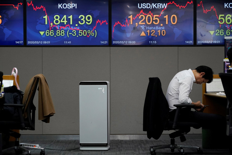 Image: A currency dealer looks at his mobile phone in front of electronic boards showing the Korea Composite Stock Price Index (KOSPI) and the exchange rate between the U.S. dollar and South Korean won, at a dealing room of a bank in Seoul
