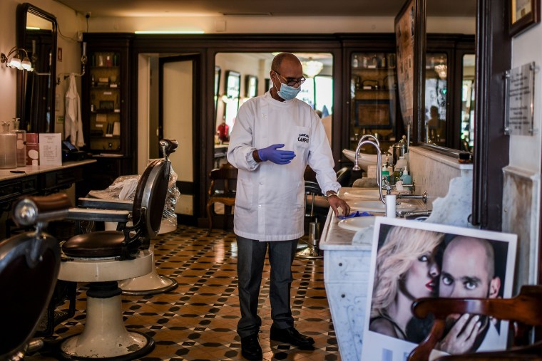 Image: Barber Elizio da Silva Gomes wearing a protective mask puts on his gloves at the Campos barbershop in Lisbon