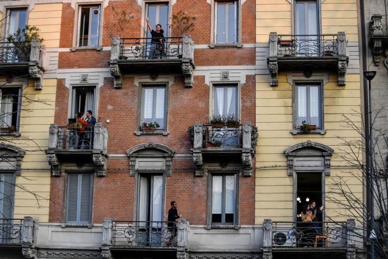 Image: People stand on their balconies to "gather" after a nationwide lockdown to slow the spread of coronavirus in Milan, Italy, on March 15, 2020. Some Italians are showing signs of solidarity by playing music for neighbors on other balconies for entert