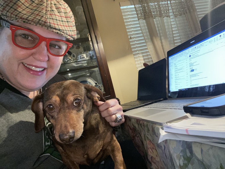 A woman hugs a dog in front of a computer.