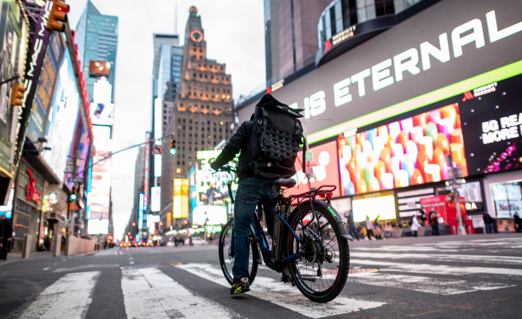 A food delivery man crosses the street in Times Square in Manhattan on March 17, 2020 in New York City. - Food delivery workers have become essential in New York after the city closed restaurants and bars to the public on March 16th, 2020. The coronavirus outbreak has transformed the US virtually overnight from a place of boundless consumerism to one suddenly constrained by nesting and social distancing.