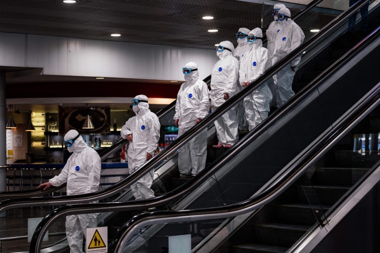 Image:  Medical staff wearing protective suits ride down an escalator at Moscow's Sheremetyevo Airport