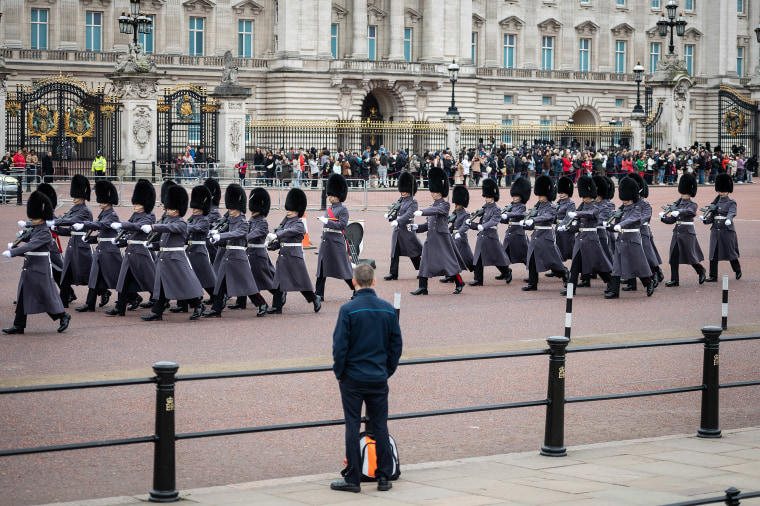 Image: A man watches the Changing of the Guard ceremony outside Buckingham Palace on the day that Queen Elizabeth II is set to move to Windsor Palace in a bid to avoid the COVID-19 coronavirus pandemic on March 18, 2020 in London,