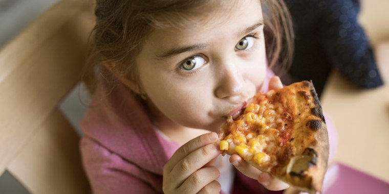 Little girl at home eating slice of pizza