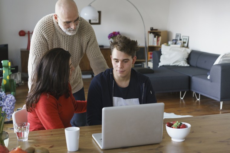 Parents talking with son by table with laptop at home