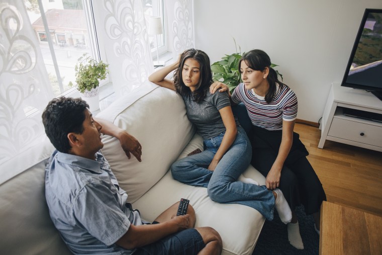 Daughters listening to father while sitting on sofa at home