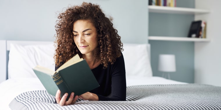 Mixed Race Woman engrossed reading a book at home on the bed in the daytime