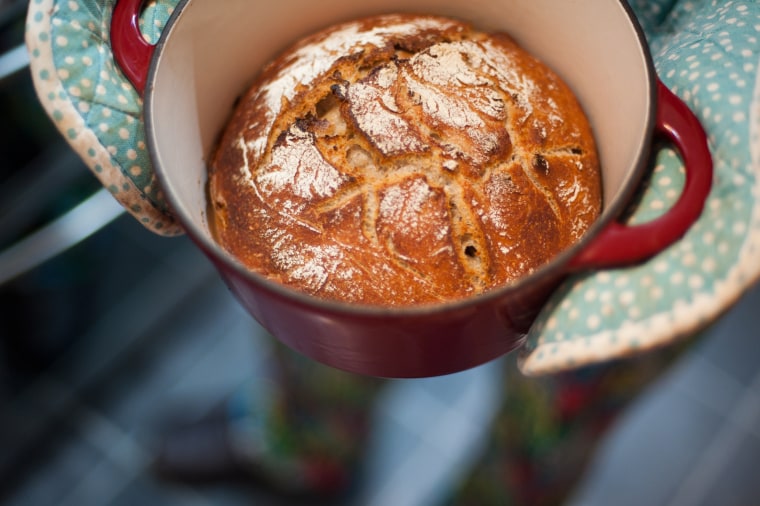 Home baked bread fresh out of the oven - in a dutch oven being held in oven gloves