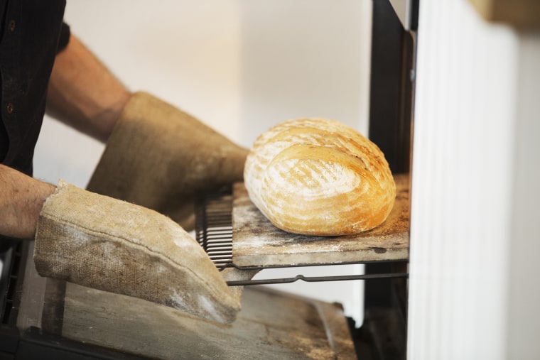 Close up of a baker taking a freshly baked loaf bread out of an oven.