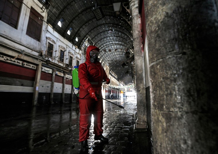 Image: A Syrian Red Crescent member sprays disinfectant along an alley of the historic Hamidiyah souk (market) in the old city of Syria's capital Damascus