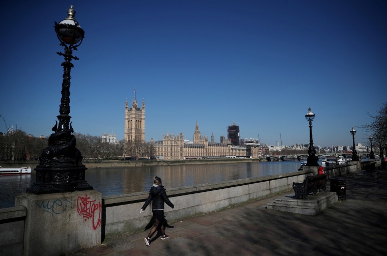 Image: A woman walks opposite the Houses of Parliament, by the River Thames, as the spread of coronavirus disease (COVID-19) continues. London,