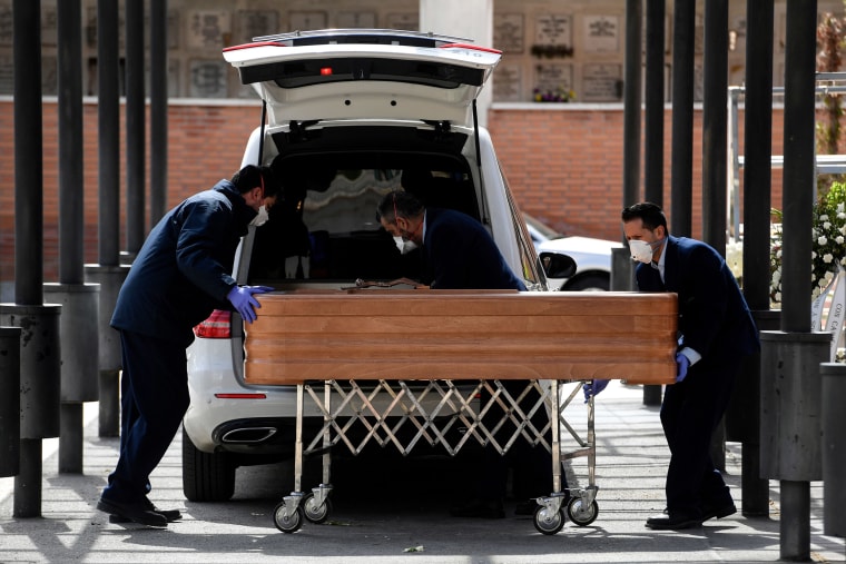 Image: Mortuary employees wearing face masks wheel a coffin into the crematorium of La Almudena cemetery in Madrid