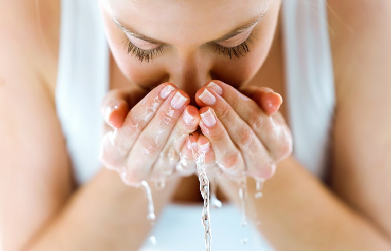 Beautiful young woman washing her face splashing water in a home bathroom.