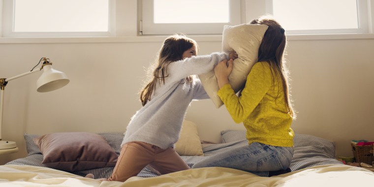 Sisters fighting with pillows on bed at home