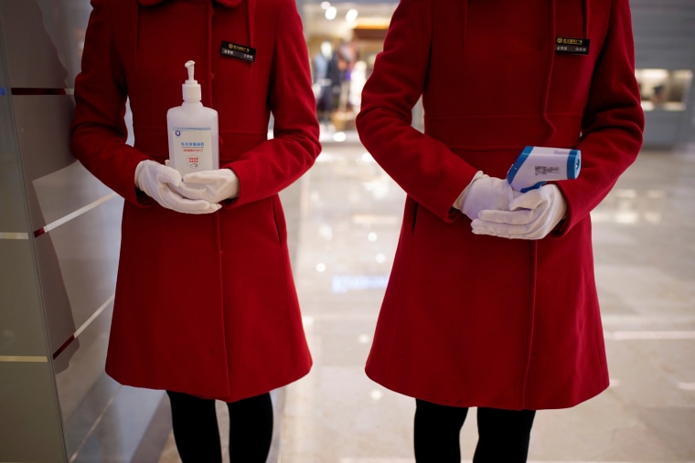 Image: Staff members of a shopping mall in Wuhan hold disinfectant gel and a thermometer at the entrance on Monday.