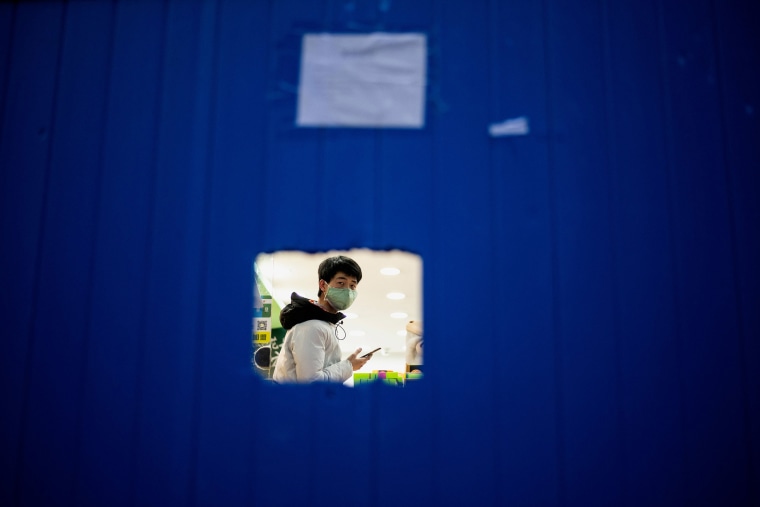 Image: A store workerwearing a wearing a facemask as a preventive measure against the COVID-19 coronavirus waits for costumers behind a barrier in Wuhan