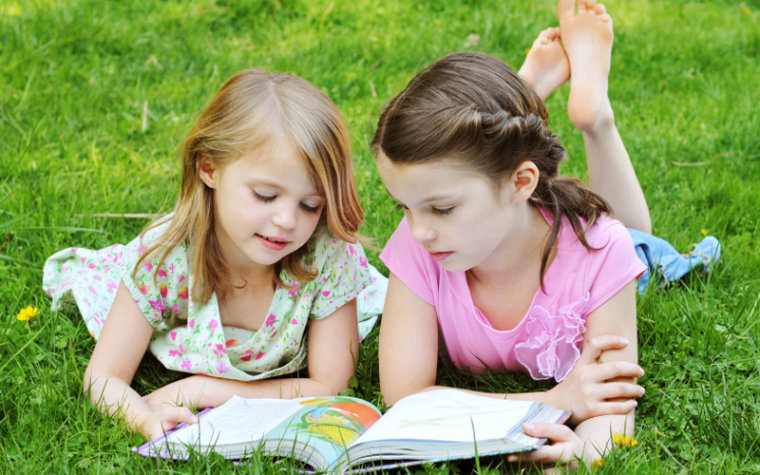 Two young girls reading in the grass.