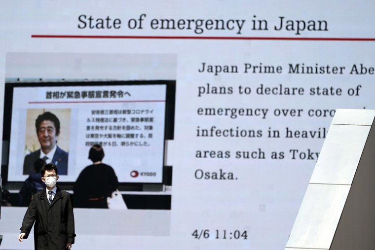 Image: A man walks past a screen in Tokyo showing a news report that Prime Minister Shinzo Abe plans to soon declare state of emergency on Monday.