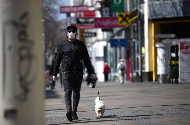 Image: A man wearing a protective mask walks a dog on a shopping street during the global coronavirus disease (COVID-19) outbreak in Vienna