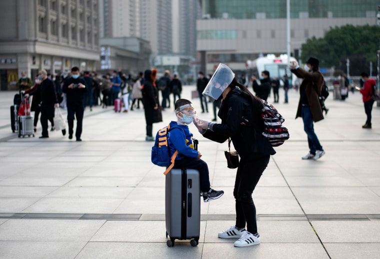 Image: A woman wearing a face mask adjusts her child's mask as they arrive at Hankou Railway Station in Wuhan to take one of the first trains leaving the city in China's central Hubei province