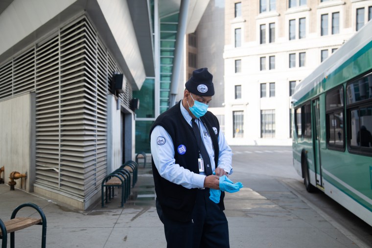 Image: A bus driver wearing a protective mask changes gloves at the Rosa Parks Transit station in Detroit