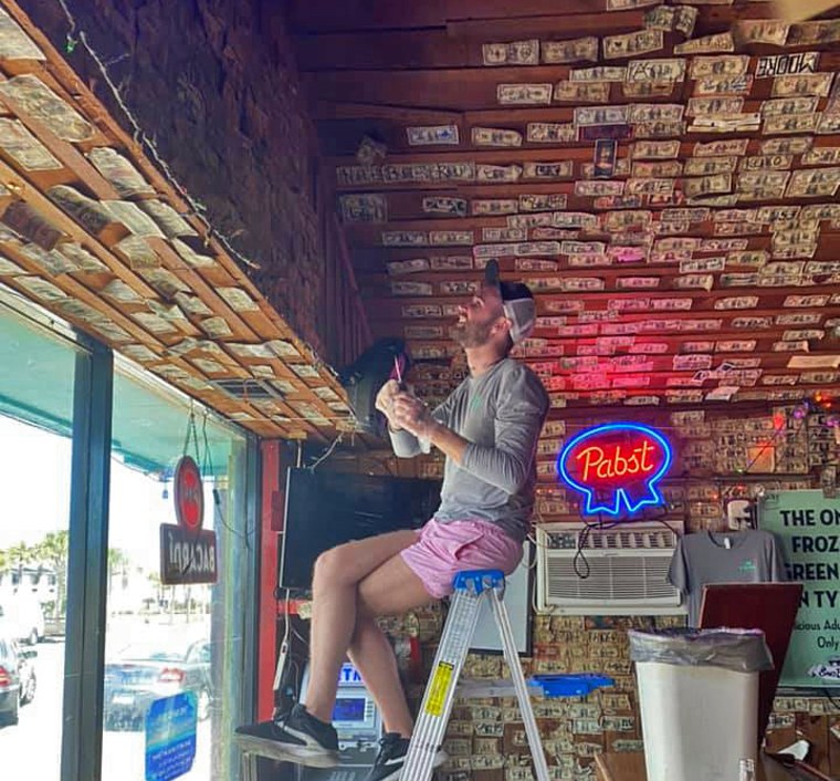 Gage McKnight, a frequent patron and friend of The Sand Bar in Tybee Island, Georgia removes dollar bills from the walls to donate to staff and community members.