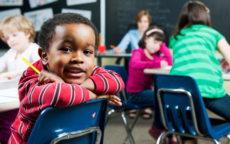Boy in striped red shirt in classroom sitting backwards on chair
