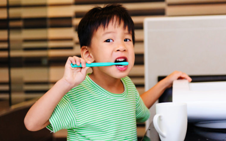 Boy in green and white striped shirt brushing teeth with blue toothbrush
