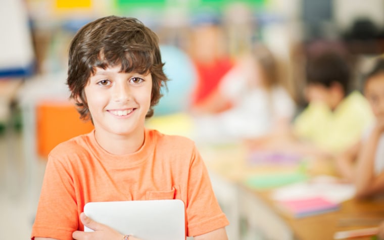Brunette boy in orange shirt holding laptop in classroom