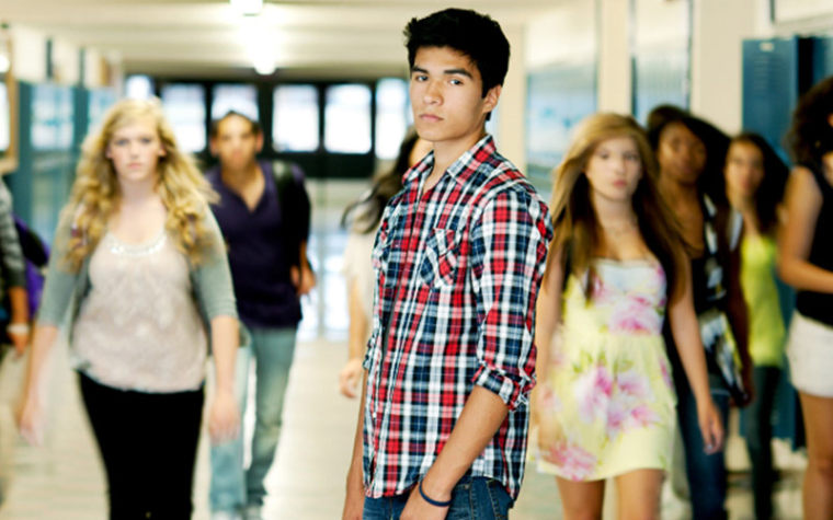 Teenage boy looks uncomfortable standing in high school hallway
