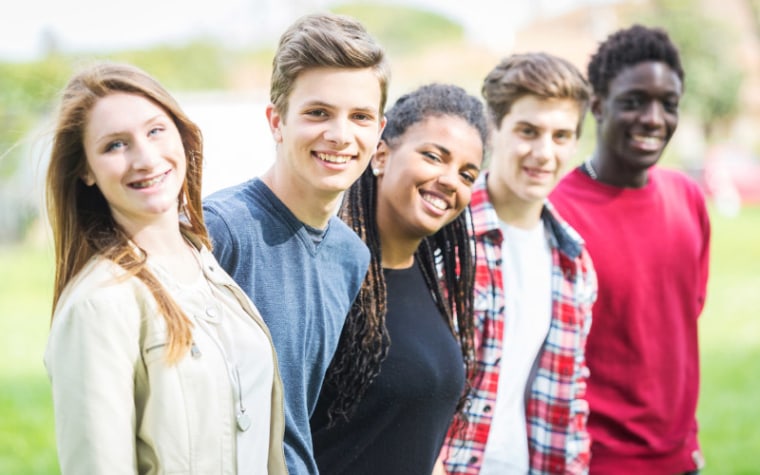 Group of teenagers standing in a line outside smiling at camera