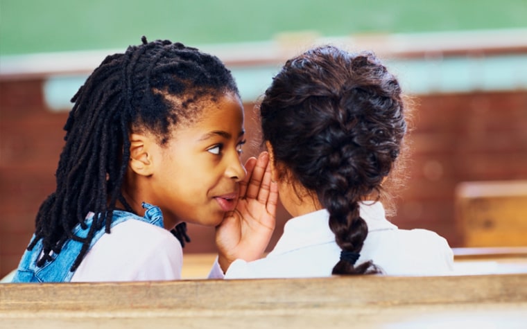 A young girl whispers into her friend's ear