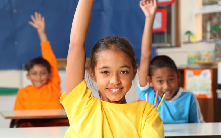 Trio of young students raise their hands in the classroom