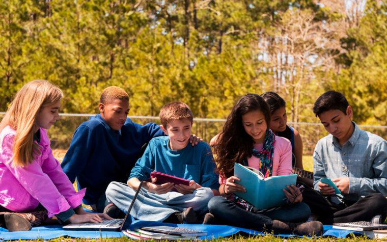 Group of preteens sitting outside reading books