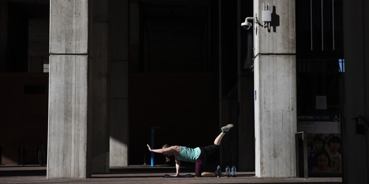 Unable to work out at her gym since it closed due to coronavirus, a woman exercises in a quiet corner at the entrance to City Hall in Boston on March 21, 2020.