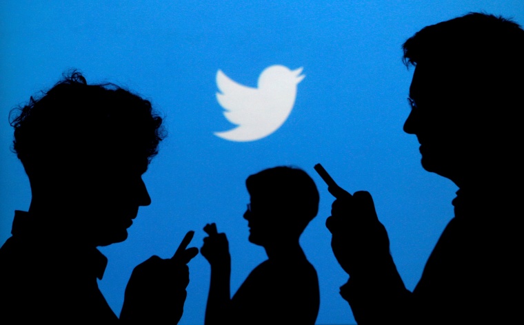 Image: People holding mobile phones are silhouetted against a backdrop projected with the Twitter logo