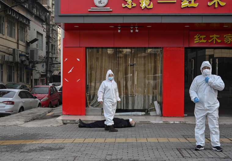 Image: Officials in protective suits check on an elderly man who collapsed and died on a street near a hospital in Wuhan