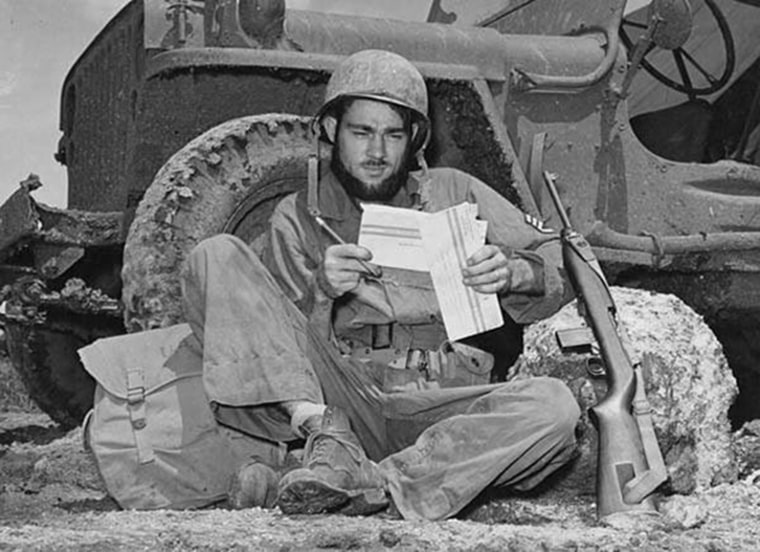 Propped against the wheel of his jeep, S/Sgt Dale Blakeslee of Carson City, Mich., uses a leisure minute to fill out the personal information form on his war ballot, on June 11, 1944 in the Mariana Islands.