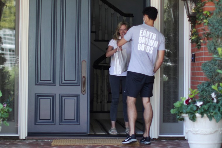 Image: Alex Brown delivers a bag for customer, Patty Pappas from The Pottery Cannabis Dispensary, as marijuana deliveries increase amid the spread of coronavirus  in Pacific Palisades