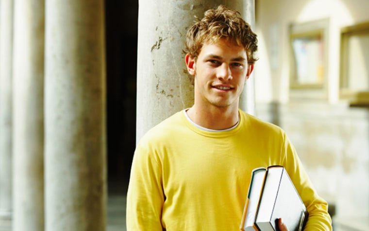 College student in yellow shirt holding textbooks while standing in a class hallway