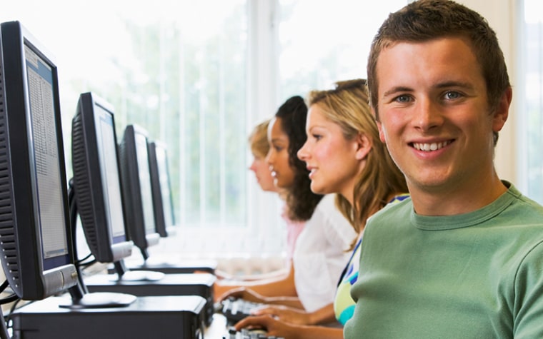 Students working on computer lab with male student in bright green shirt