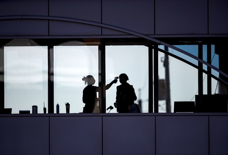 Image: Amid coronavirus concerns, a healthcare worker takes the temperature of a visitor to Essentia Health who was crossing over a skywalk bridge from the adjoining parking deck, Friday, April 10, 2020, in Duluth, Minn